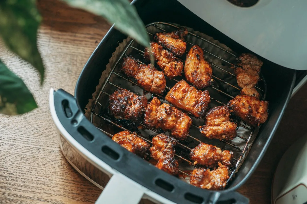 Open airfryer met een mand vol knapperig gebakken kipstukjes op een houten tafel