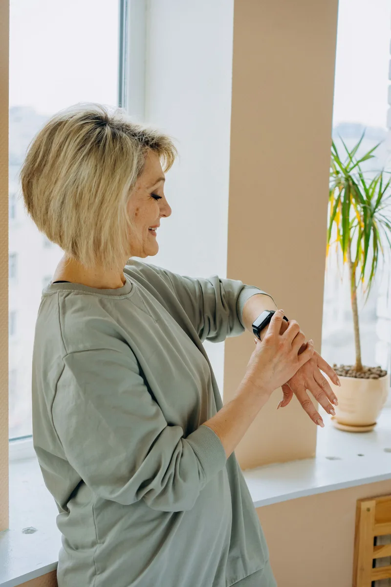 Oudere vrouw kijkt bij het raam naar het horloge om haar pols