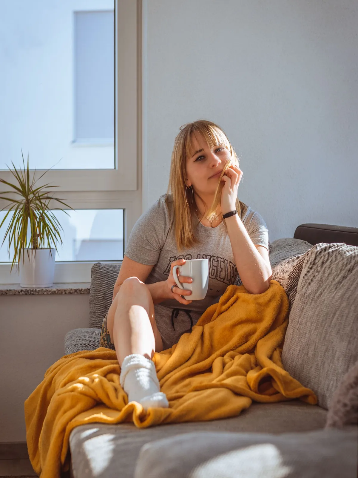 Vrouw met een mok op de bank onder een gele fleecedeken