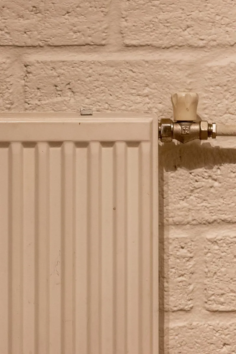 Witte paneelradiator met thermostaatkraan tegen een gestucte bakstenen buitenmuur