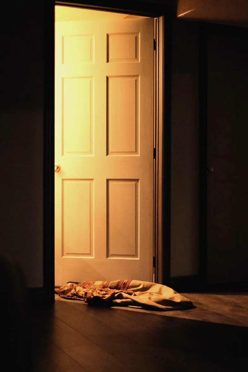Deur op een kier met warm licht erachter en een deken als tochtweerder op de vloer