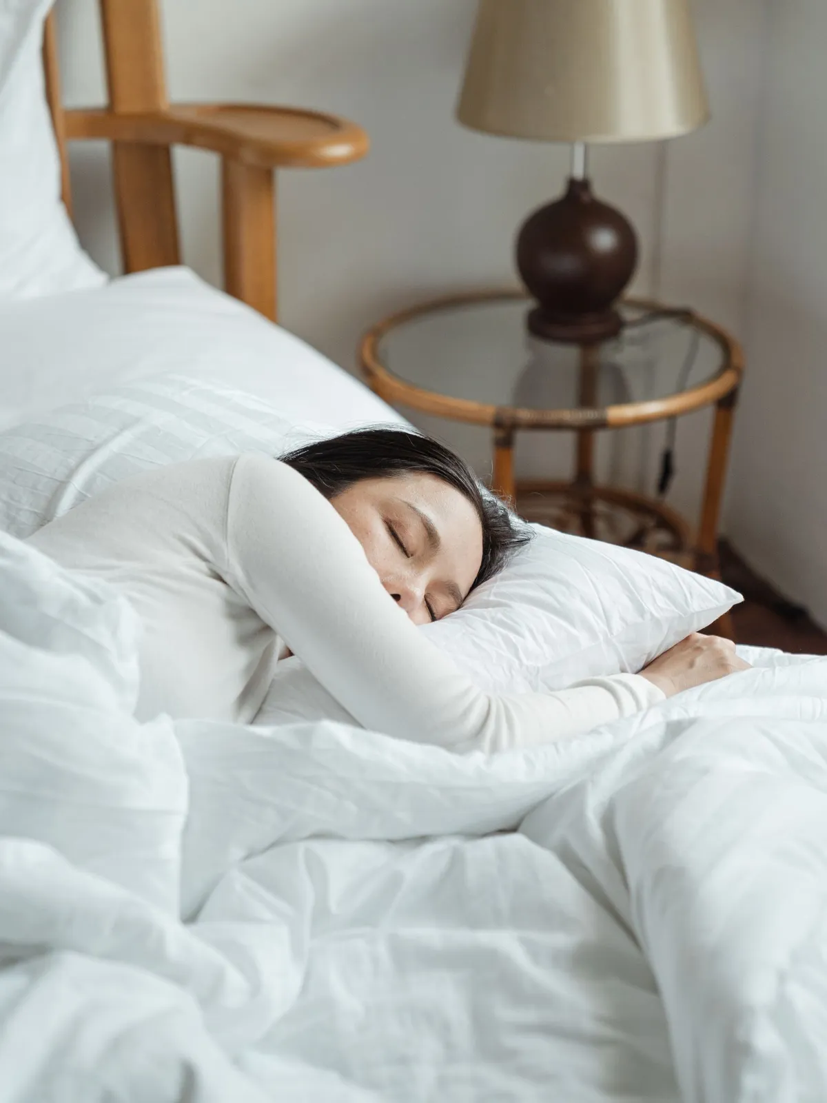 Vrouw slaapt op haar zij op een wit hoofdkussen in een opgemaakt bed