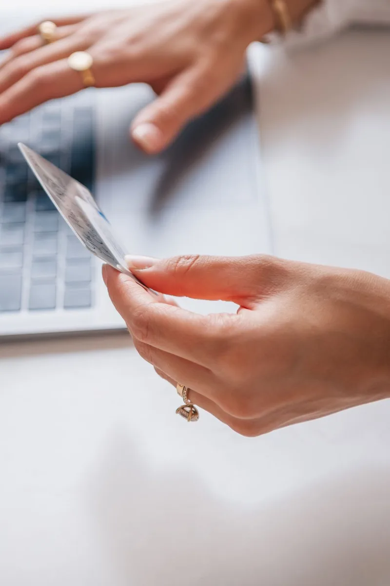 Handen houden een bankpas vast boven een laptoptoetsenbord tijdens het online winkelen
