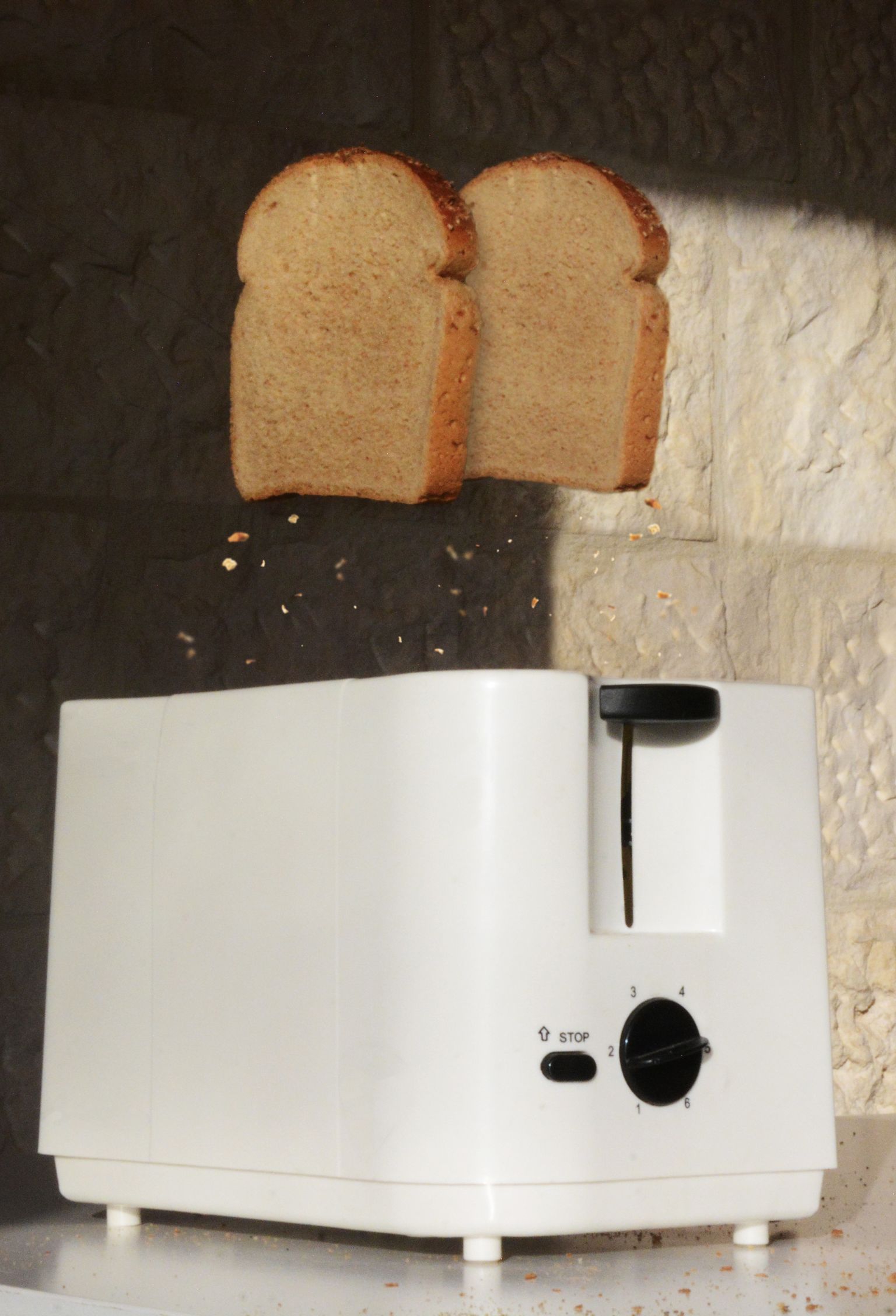 Twee sneden bruinbrood springen met kruimels uit een witte broodrooster