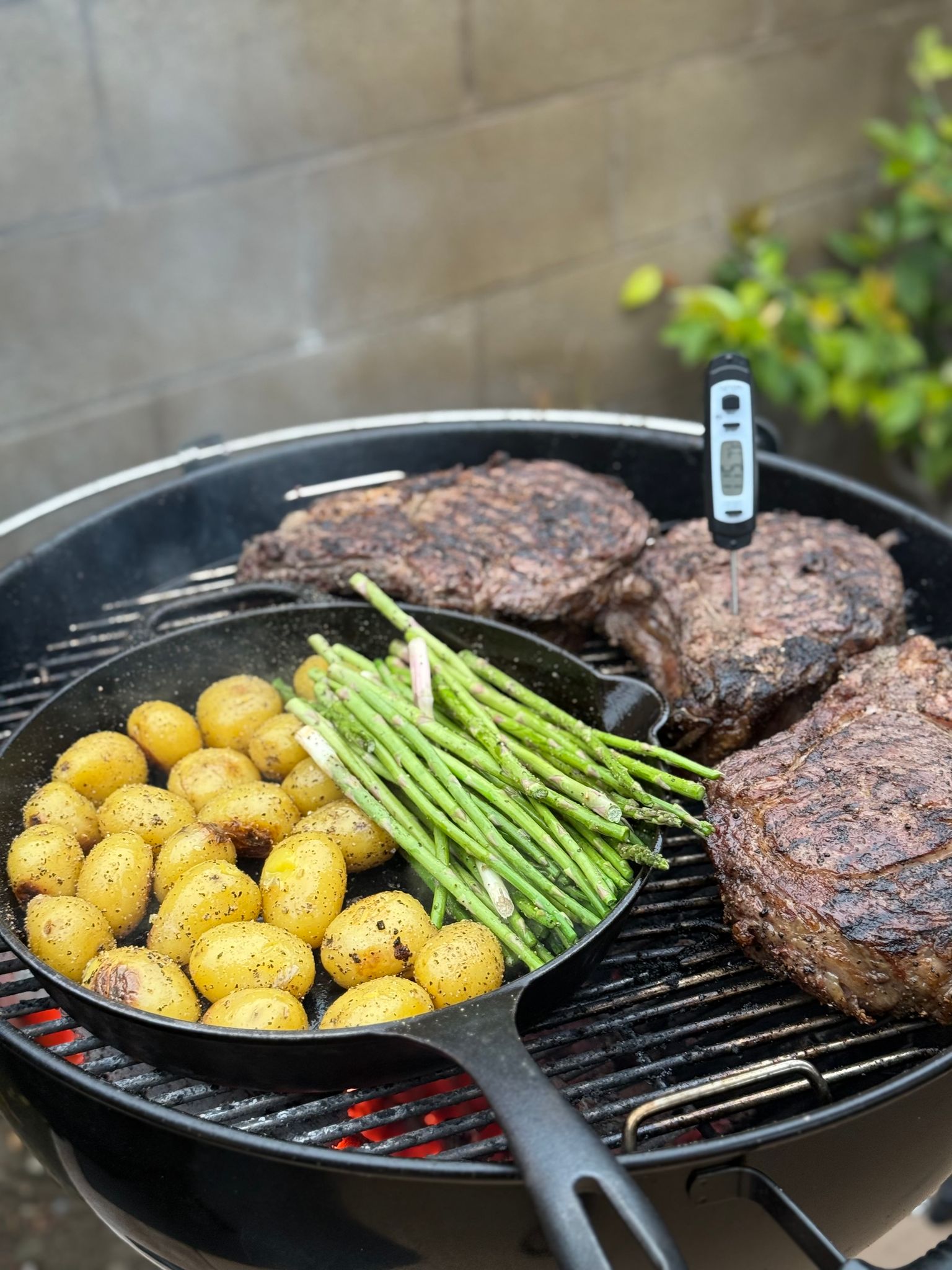 Biefstukken en aardappeltjes op een barbecue met een vleesthermometer in het vlees