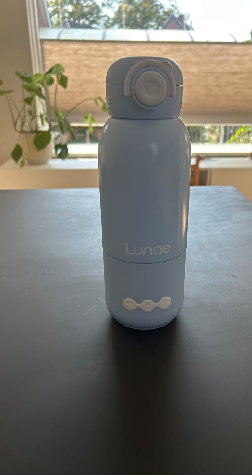 Lunae flessenwarmer op een tafel, met de drie knoppen onderaan en de draaglus op de dop