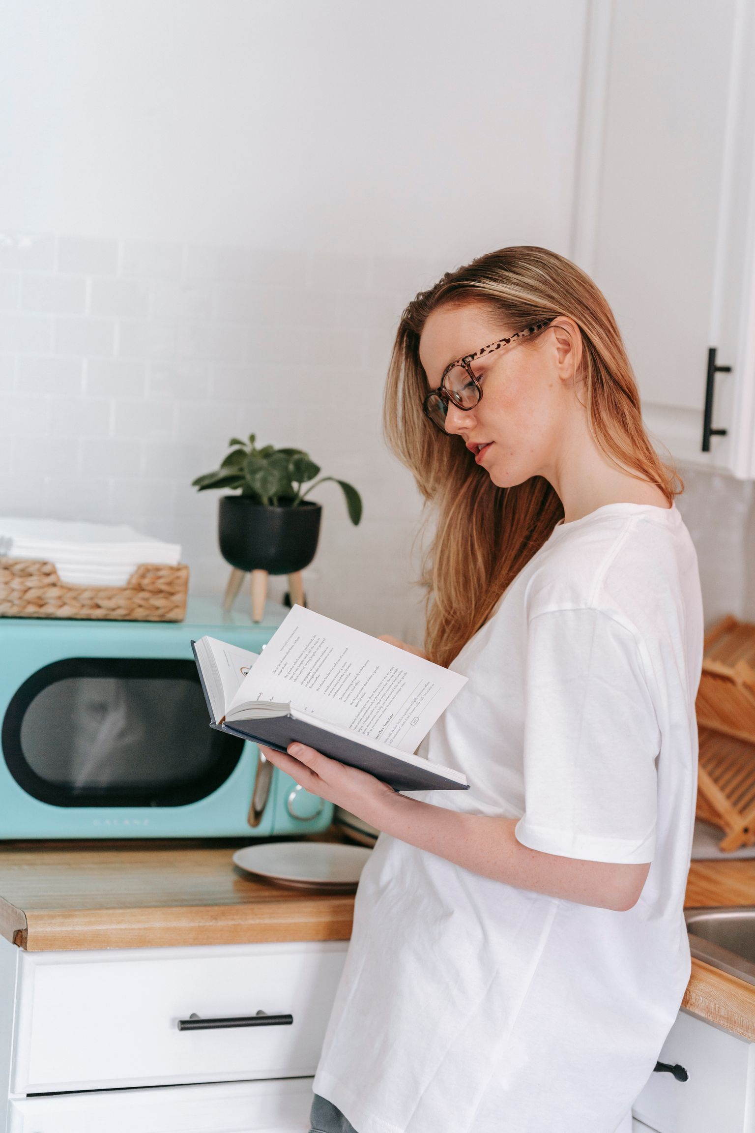 Vrouw leest een kookboek in een lichte keuken met een mintgroene magnetron op het aanrecht