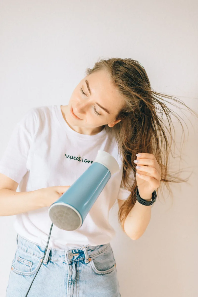 Vrouw föhnt haar lange haar met een lichtblauwe haardroger