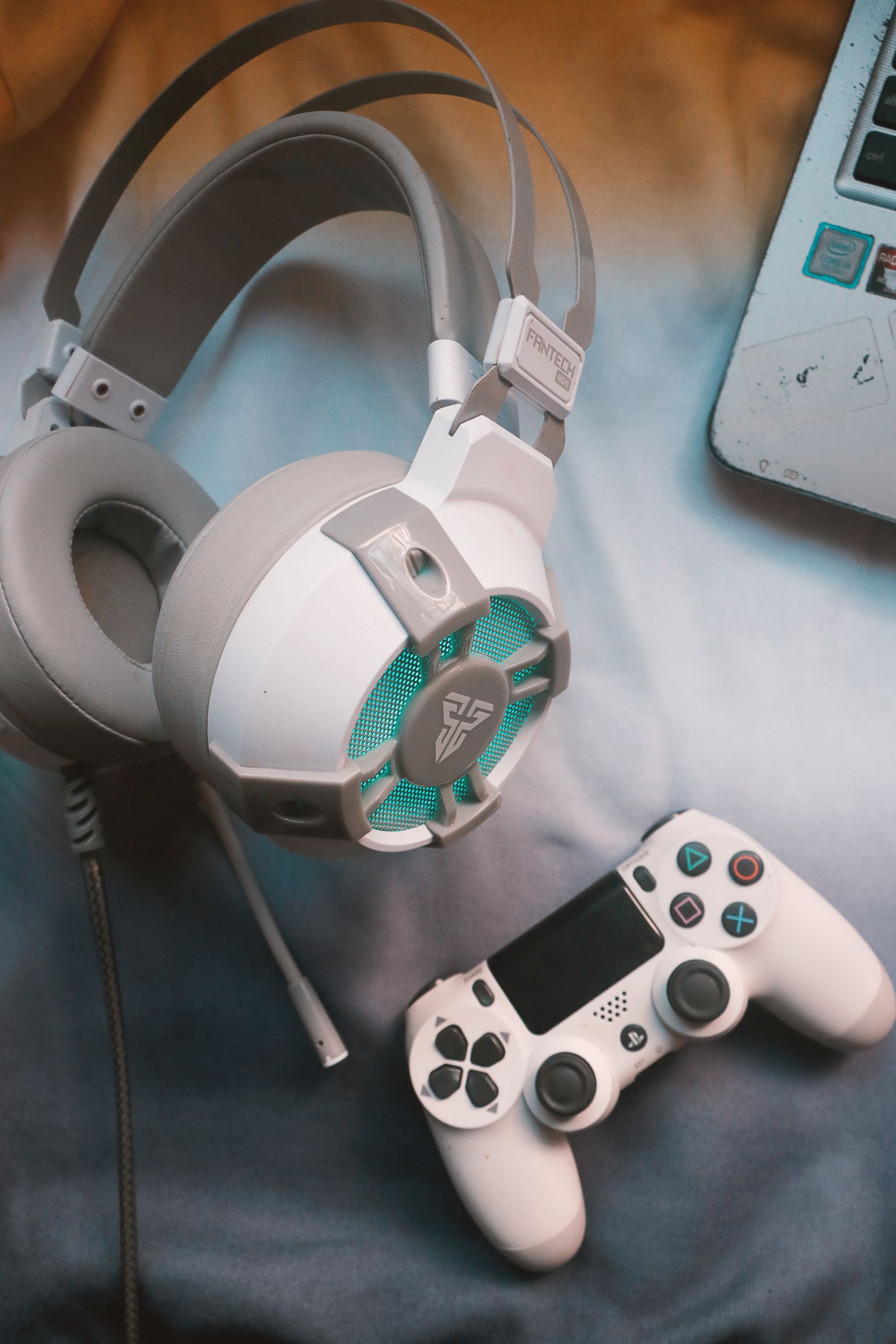 Witte gaming headset naast een witte controller en een laptop op een blauwe ondergrond