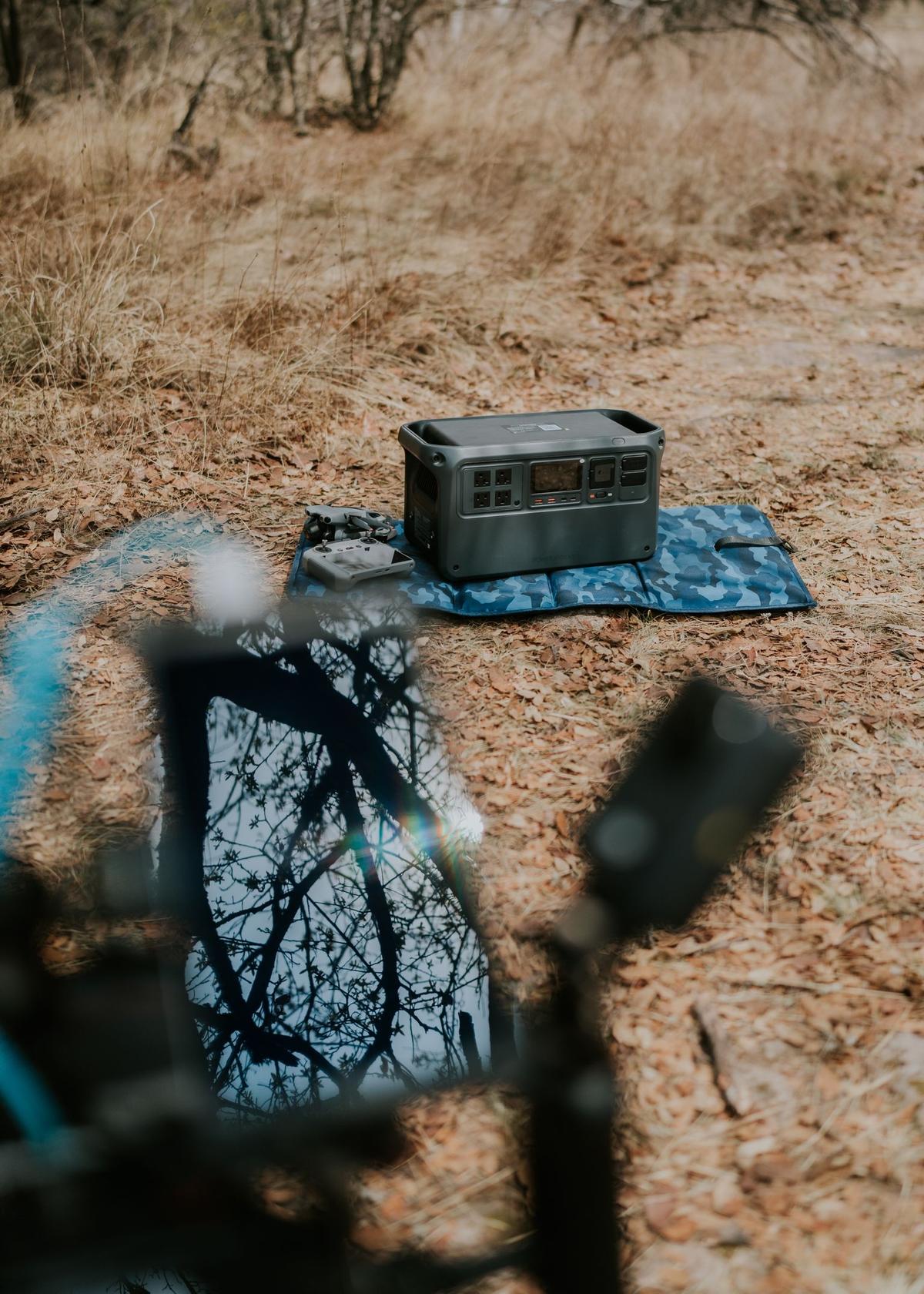 Draagbaar powerstation met stopcontacten en display op een deken in de natuur, naast een drone en afstandsbediening