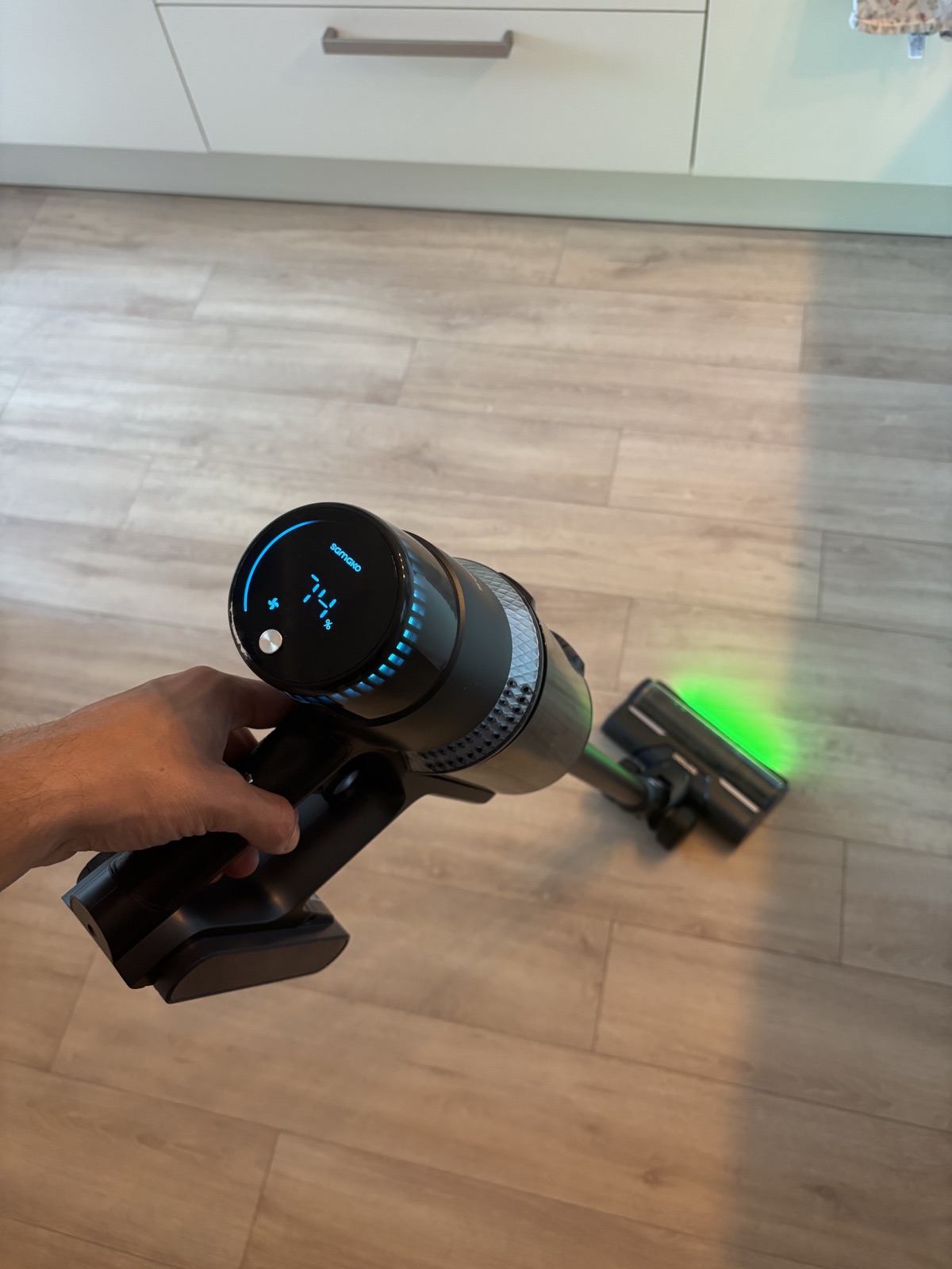 Samako CleanDetect in de hand met blauw verlicht display en de groene LED-verlichting die de vloer voor de borstelkop verlicht