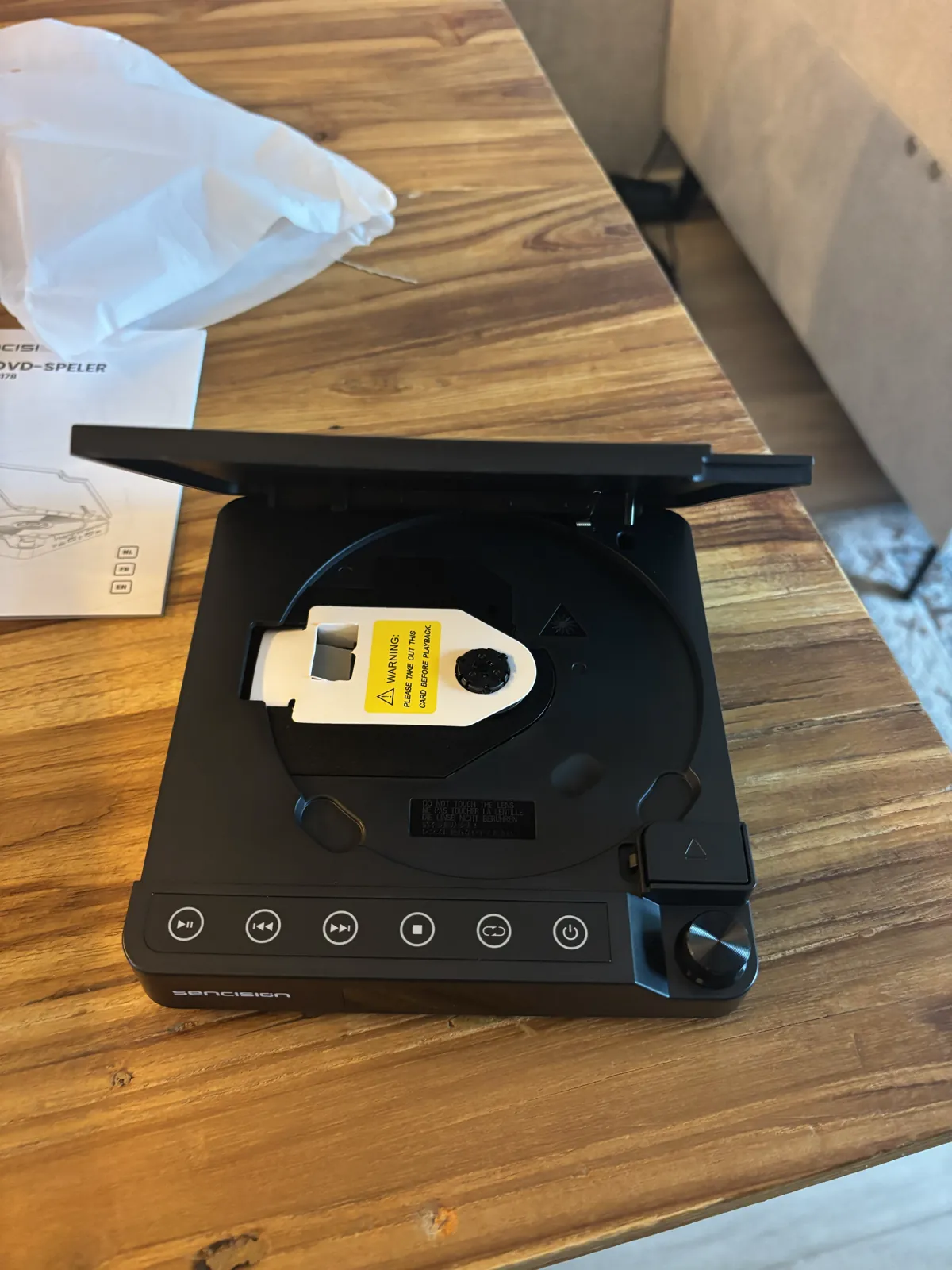 Sencision mini dvd-speler met open klep, het gele transportkaartje op de disc-houder en de rij bedieningsknoppen aan de voorkant