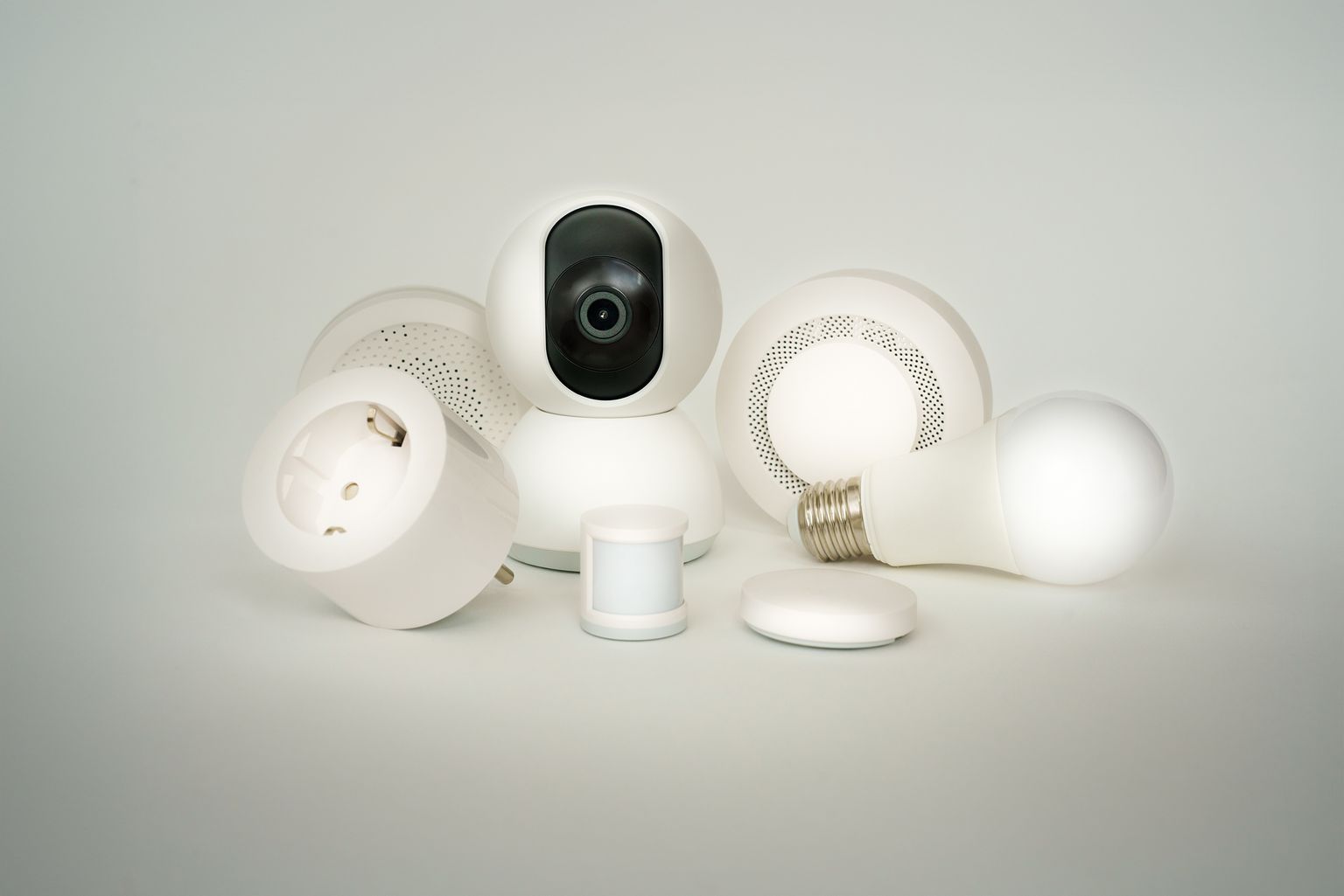 Witte slimme stekker naast andere smart home-apparaten zoals een beveiligingscamera, bewegingssensor en slimme lamp