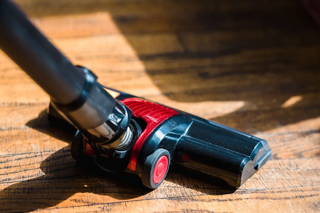 Steelstofzuiger met rood mondstuk op een houten vloer in het zonlicht