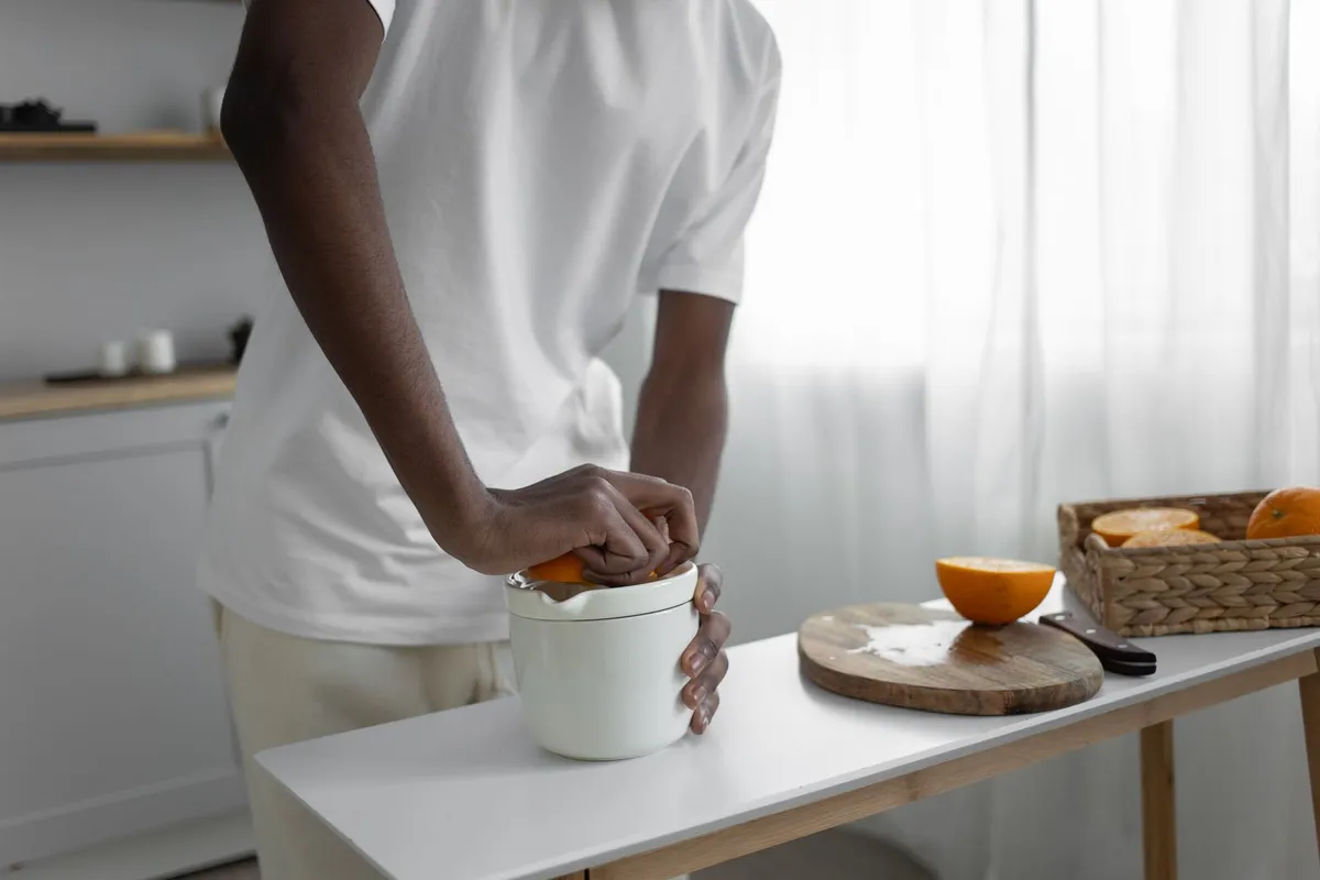 Man perst een halve sinaasappel op een witte citruspers in een lichte keuken