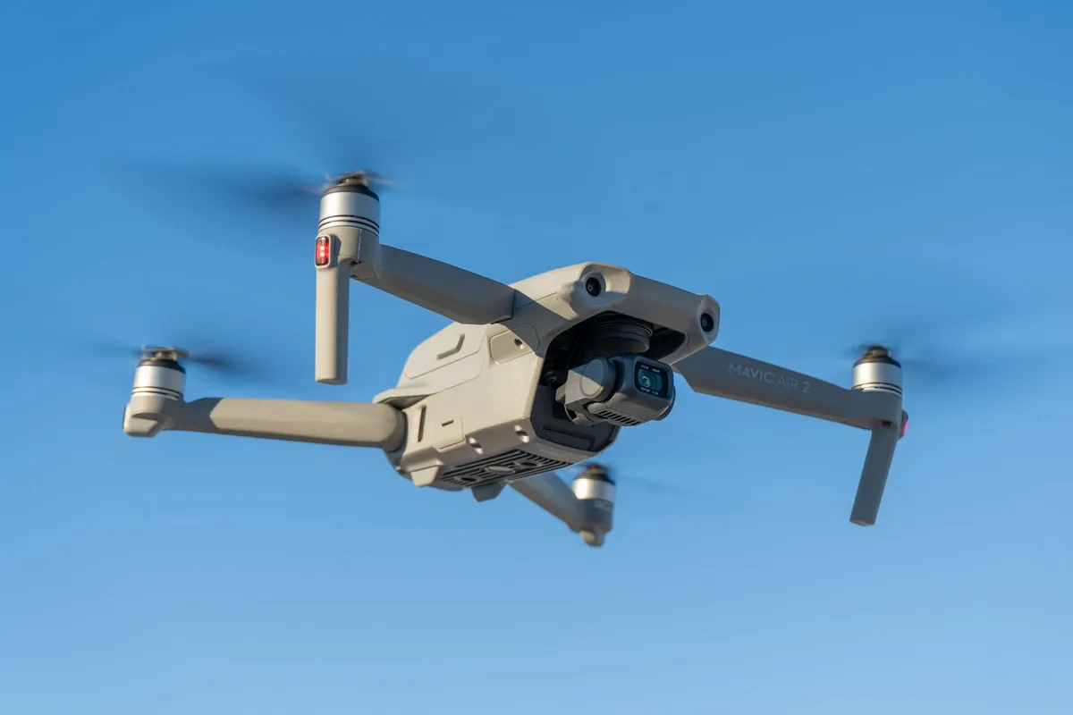 Kleine grijze drone met camera vliegt tegen een blauwe lucht