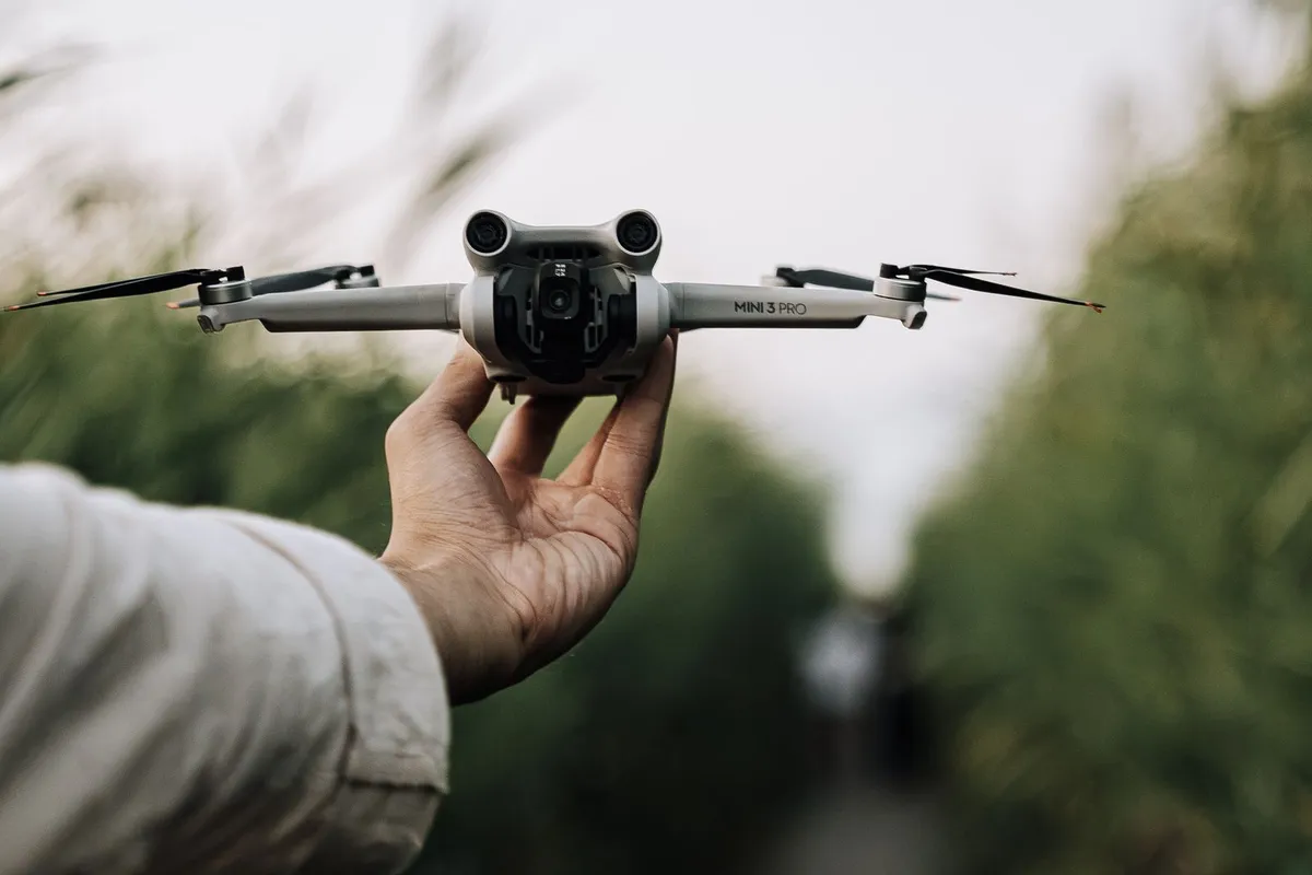 Hand houdt een compacte opvouwbare drone onder de 249 gram vast, met afstandsbediening op de voorgrond
