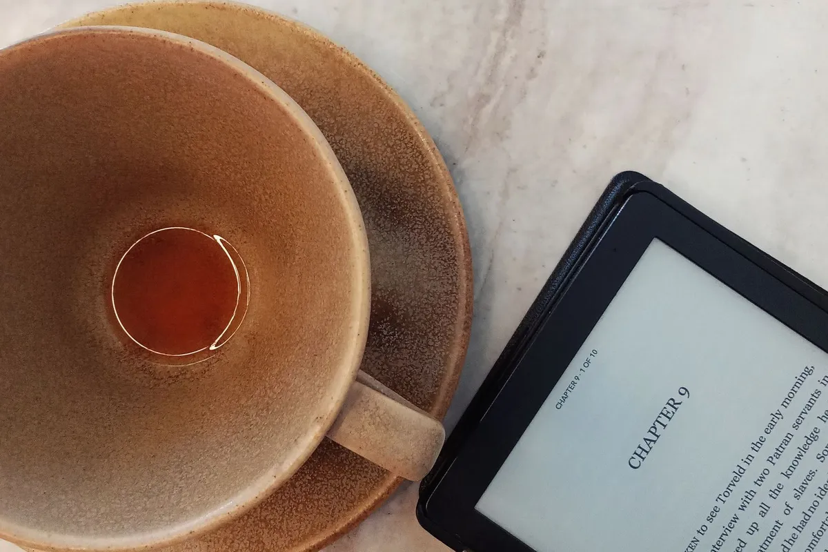 E-reader met geopend boek naast een kop thee op een marmeren tafel