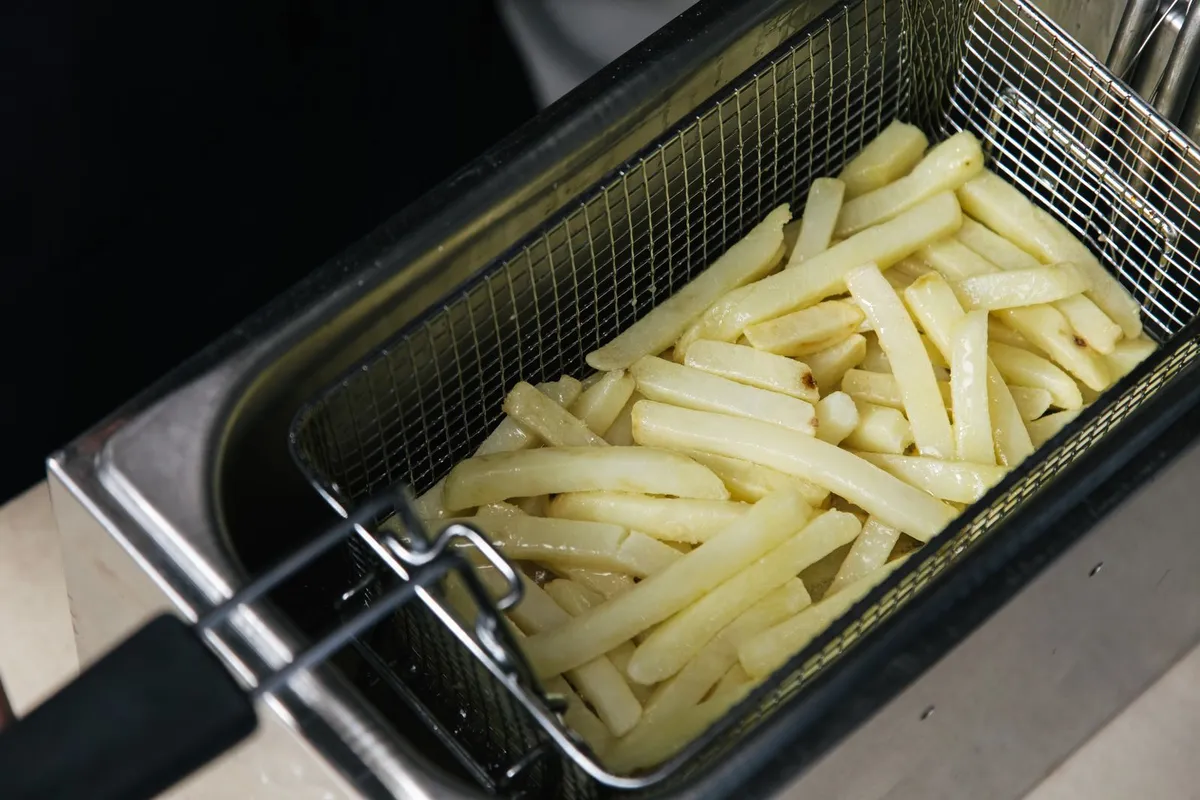 Frietmand vol rauwe friet boven een roestvrijstalen frituurpan