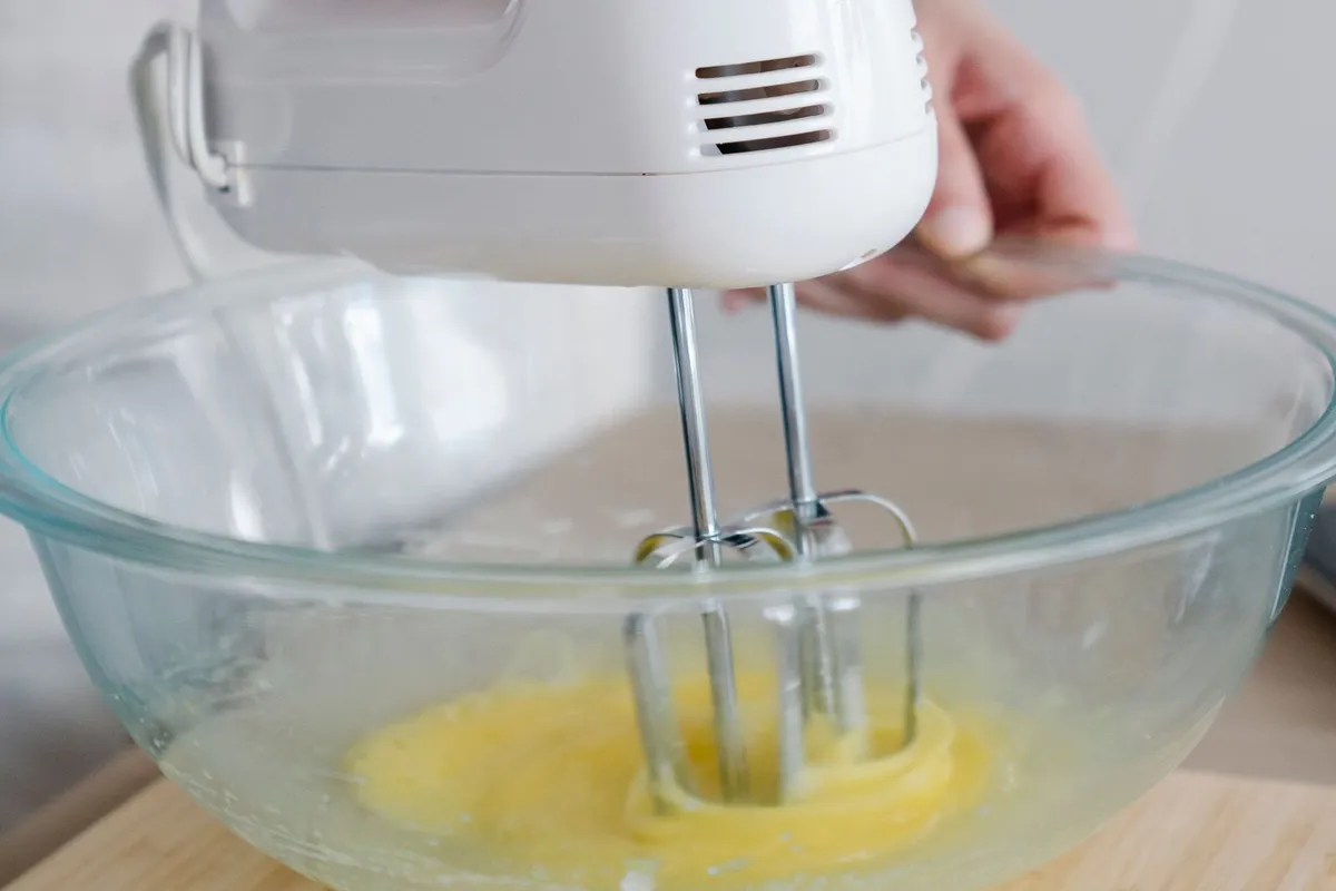 Witte handmixer met gardes klopt eieren in een glazen kom