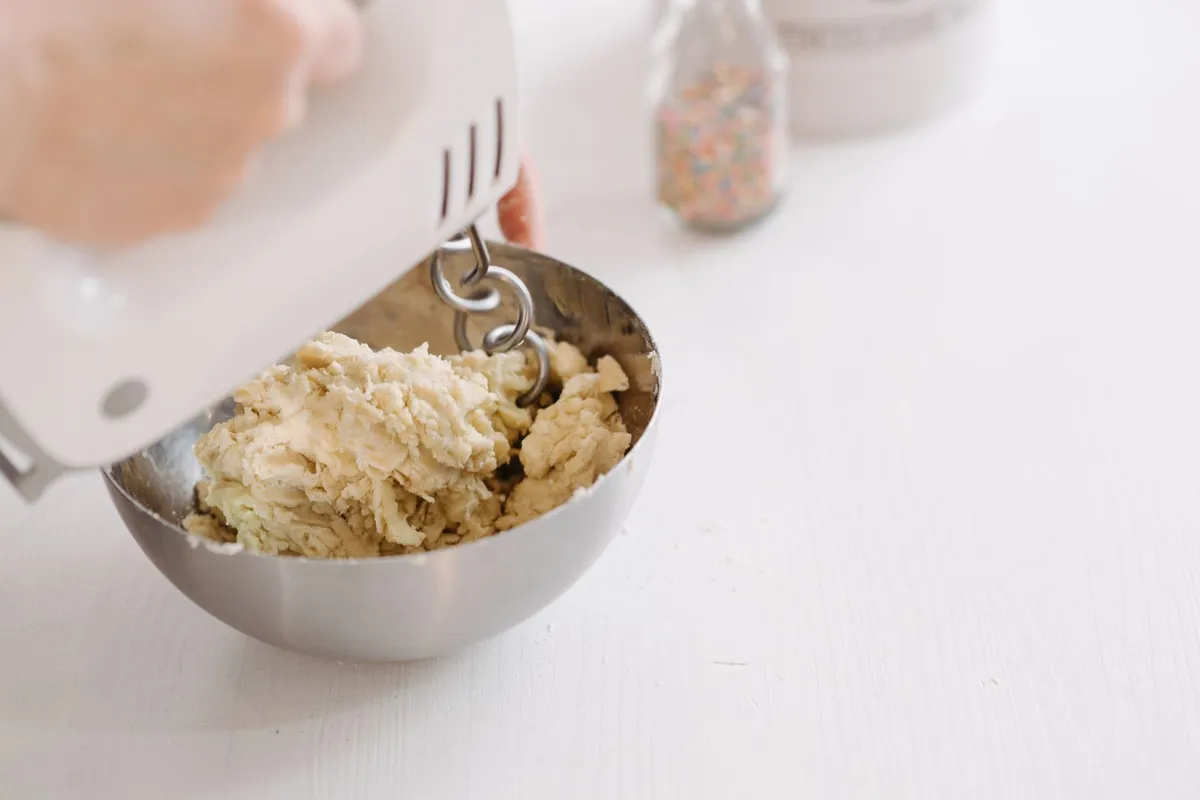 Handmixer met deeghaken kneedt stevig koekjesdeeg in een metalen kom