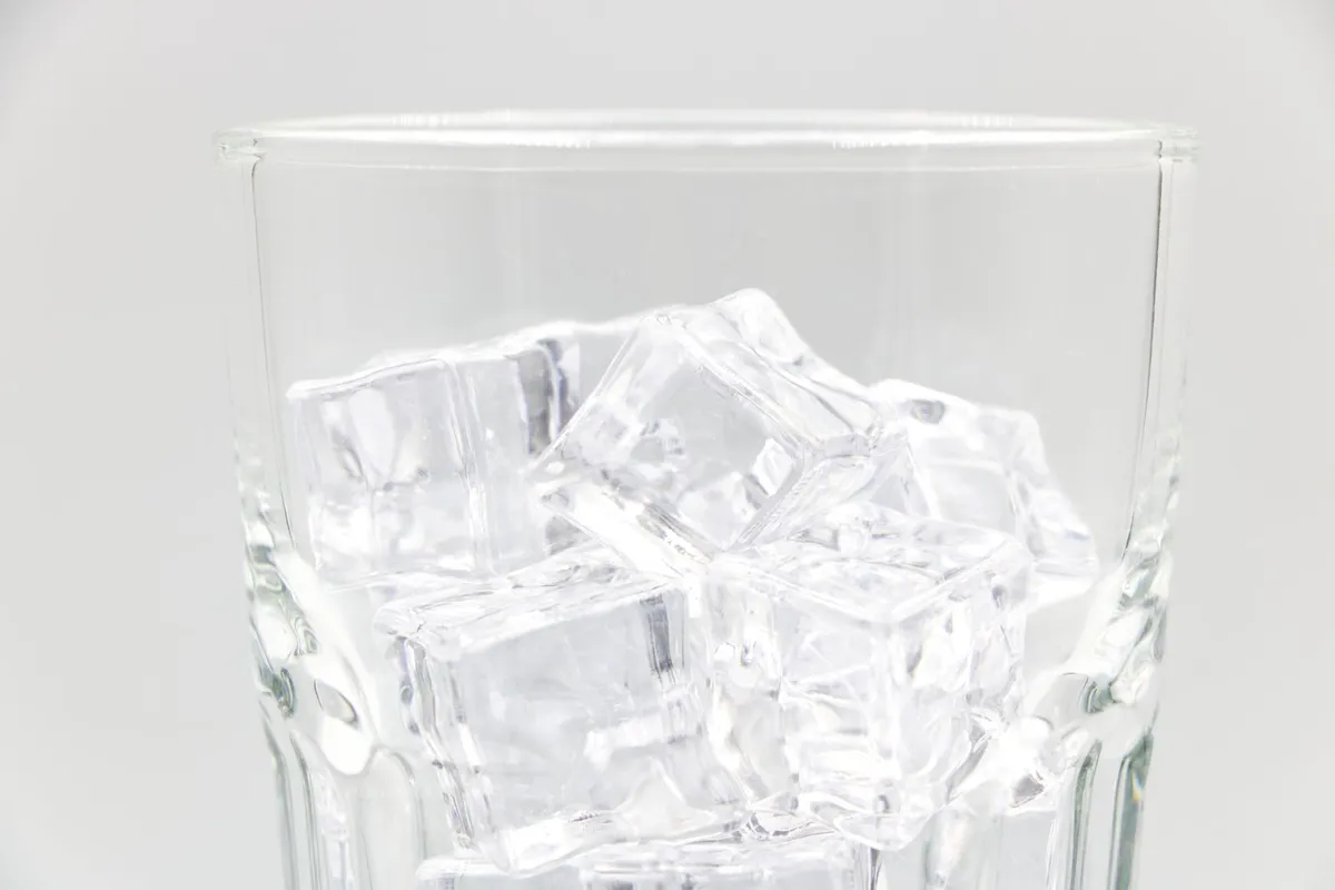 Glas gevuld met vierkante heldere ijsblokjes tegen een lichte achtergrond