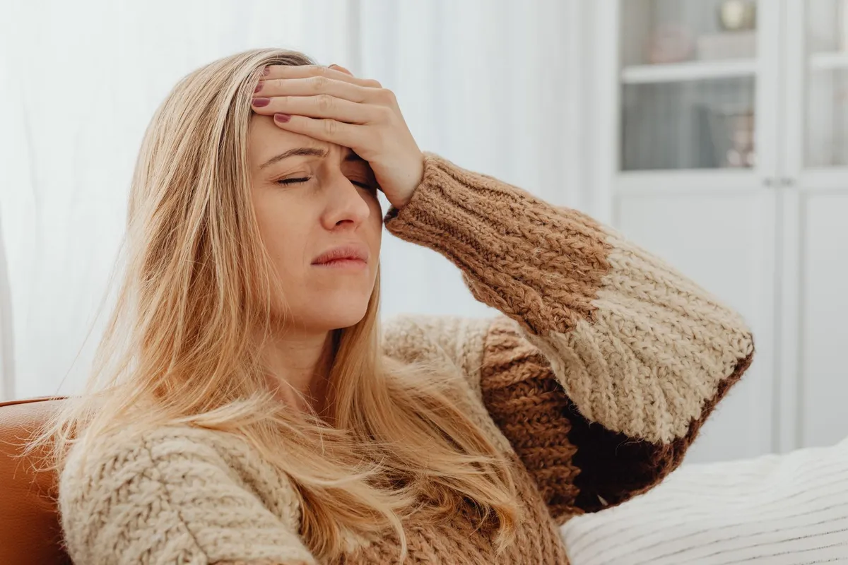 Vrouw in een gebreide trui zit op de bank met haar hand tegen haar voorhoofd