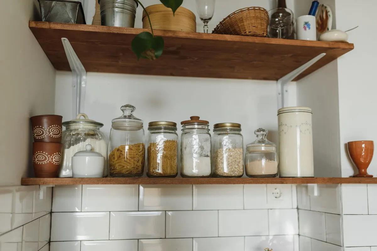 Glazen voorraadpotten met pasta en andere droge voeding op een houten plank in de keuken