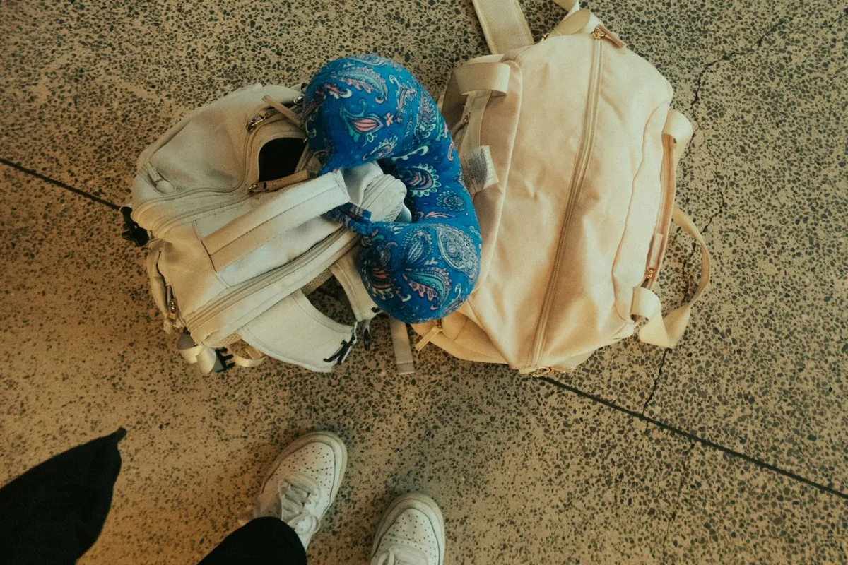 Rugzak en tas met een blauw reiskussen op de vloer van een vertrekhal