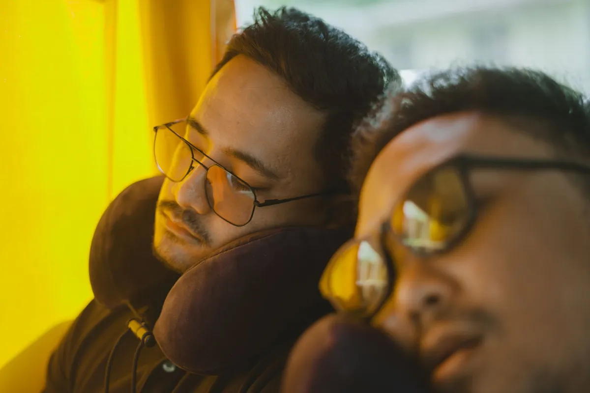Twee reizigers slapen rechtop in een bus met een reiskussen om hun nek