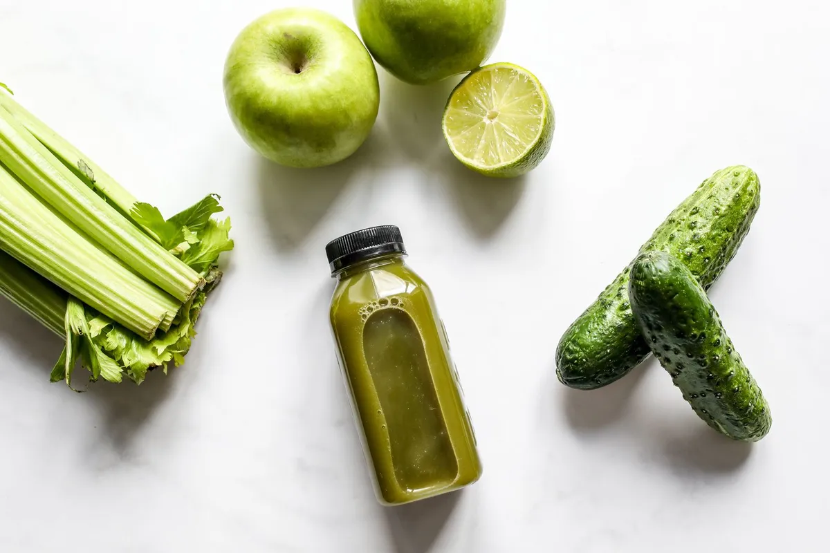 Fles groen sap met appels, limoen, selderij en komkommers op een wit blad
