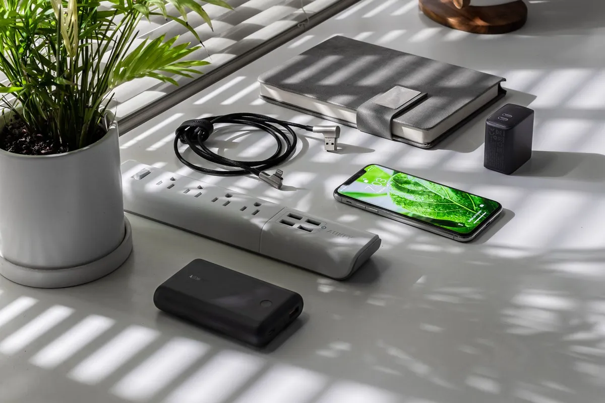Witte stekkerdoos met USB-poorten op een bureau naast een telefoon, powerbank en plant