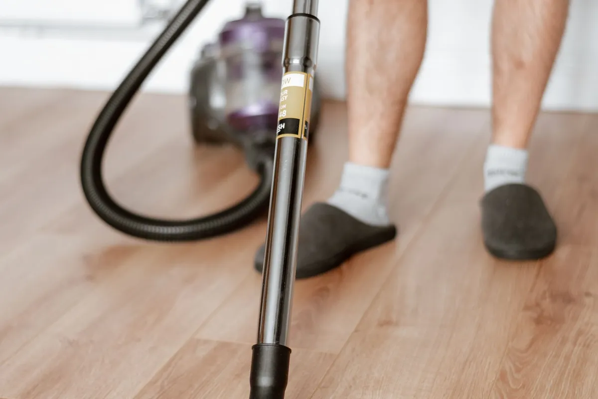 Man stofzuigt een houten vloer met een sledestofzuiger met slang