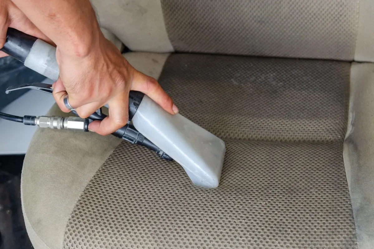 Sproei-zuigmondstuk van een vlekkenreiniger trekt vuil uit een stoffen autostoel