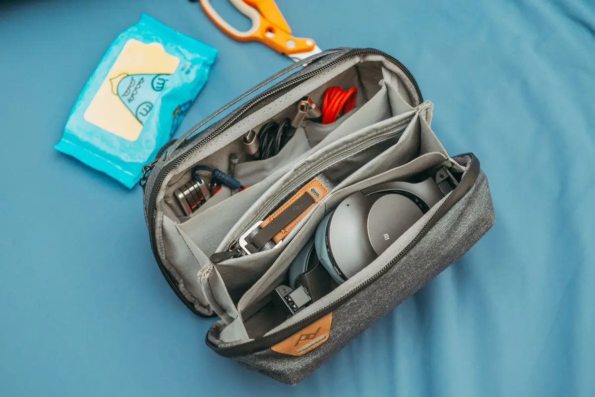 Open reistasje met koptelefoon, laadkabels en adapters op een blauw laken