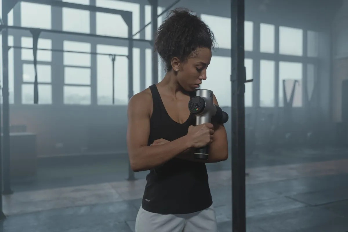 Vrouw masseert haar bovenarm met een massage gun in de sportschool