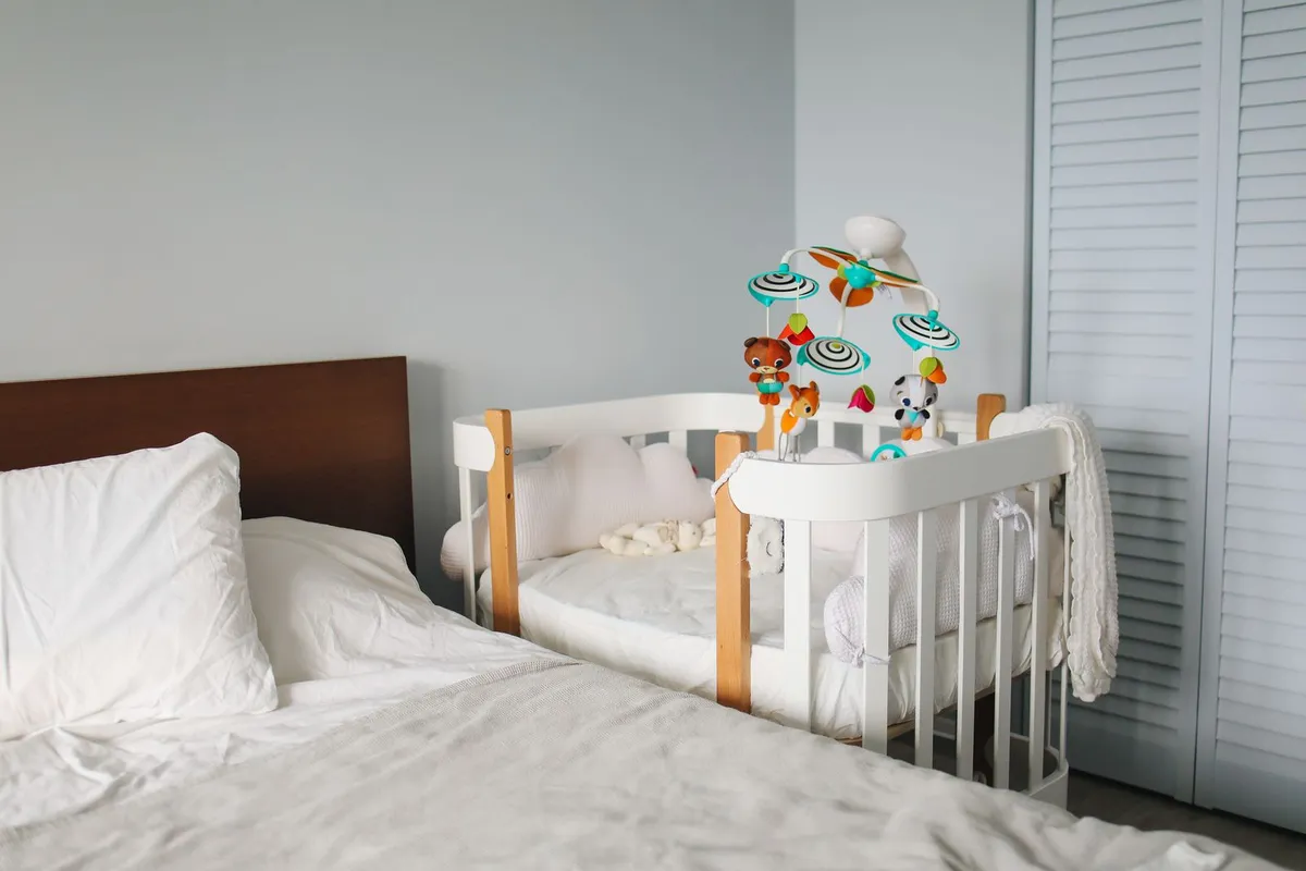 Co-sleeper met open zijkant vlak naast het ouderbed in een lichte slaapkamer