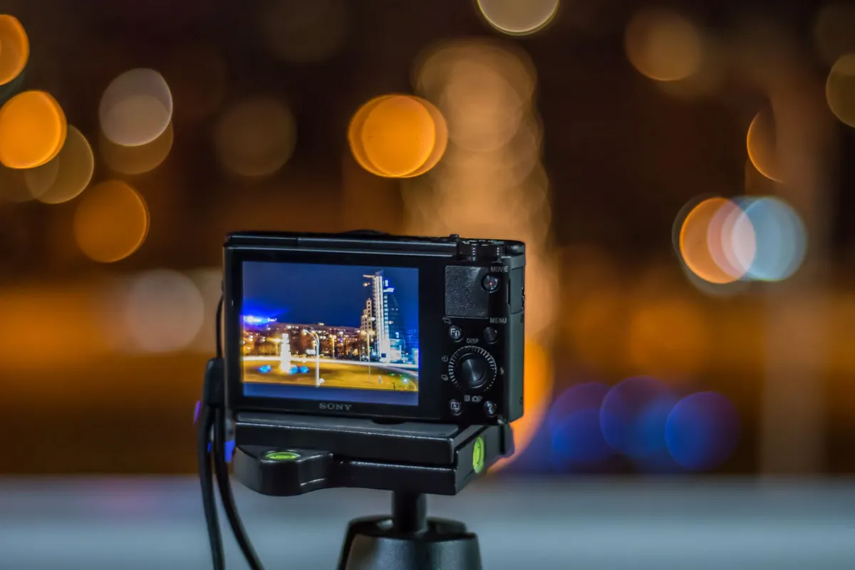 Compacte camera op een statief met een scherpe stadsfoto op het scherm, lichtjes op de achtergrond