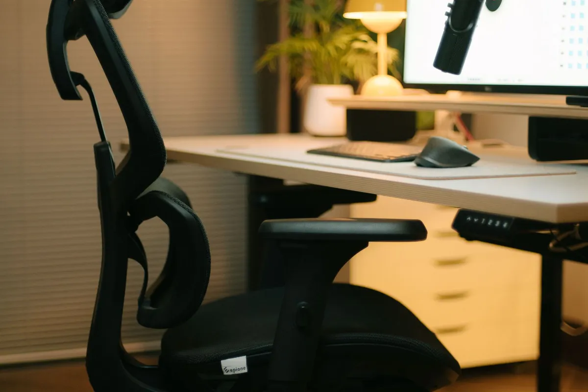Zwarte ergonomische bureaustoel met hoofdsteun, verstelbare armleuningen en mesh rugleuning bij een zit-sta-bureau