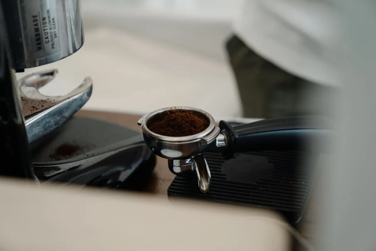 Filterhouder gevuld met vers gemalen koffie naast een koffiemolen