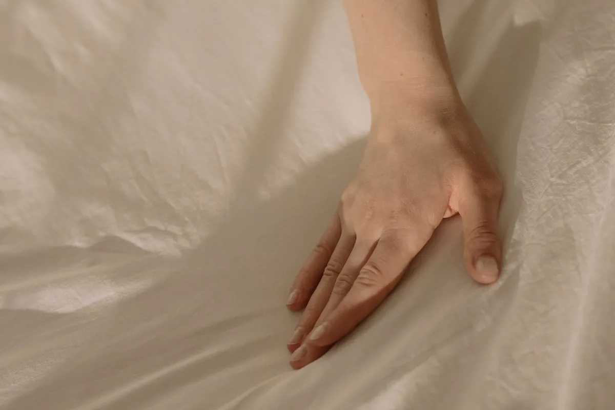 Hand drukt op een wit laken om de hardheid van het matras te voelen