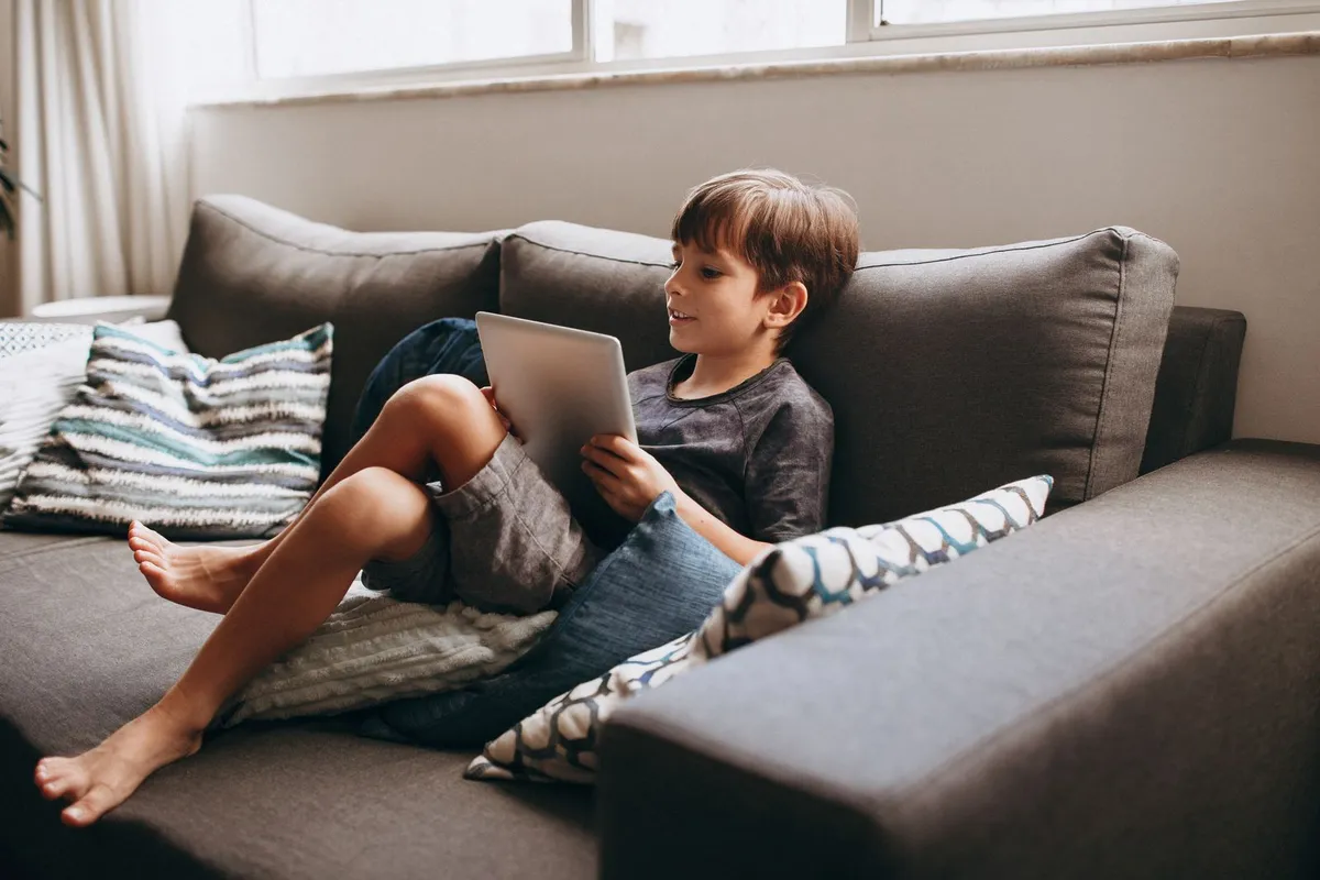 Jongen zit ontspannen op de bank met een tablet op schoot