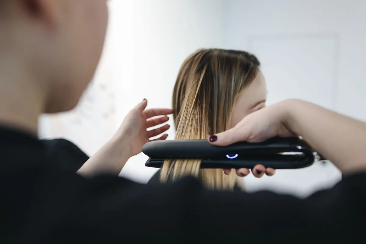 Kapper haalt een stijltang met verwarmde platen door lang blond haar
