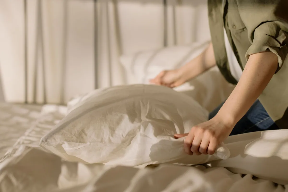 Iemand schudt een kussen op bij het opmaken van een bed met licht beddengoed
