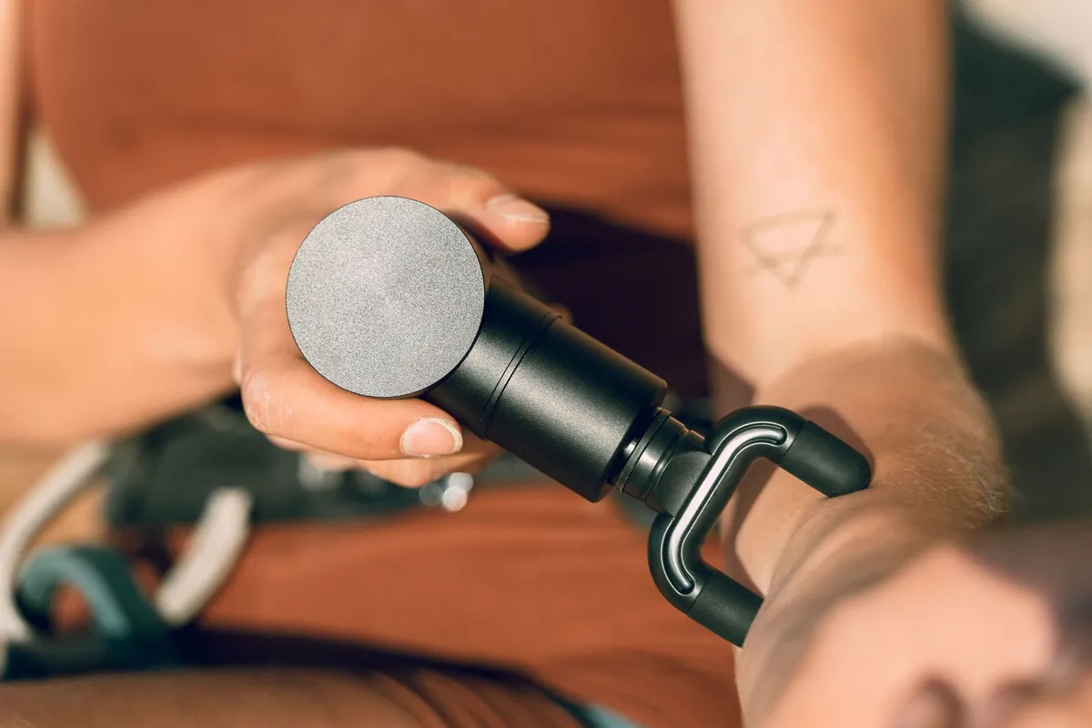 Hand houdt een massage gun vast boven een onderarm
