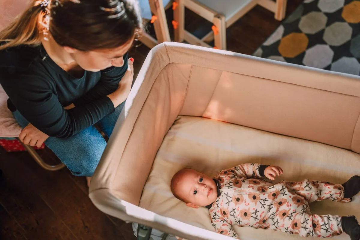 Moeder kijkt naar haar baby die op een stevig matrasje in een babybedje ligt