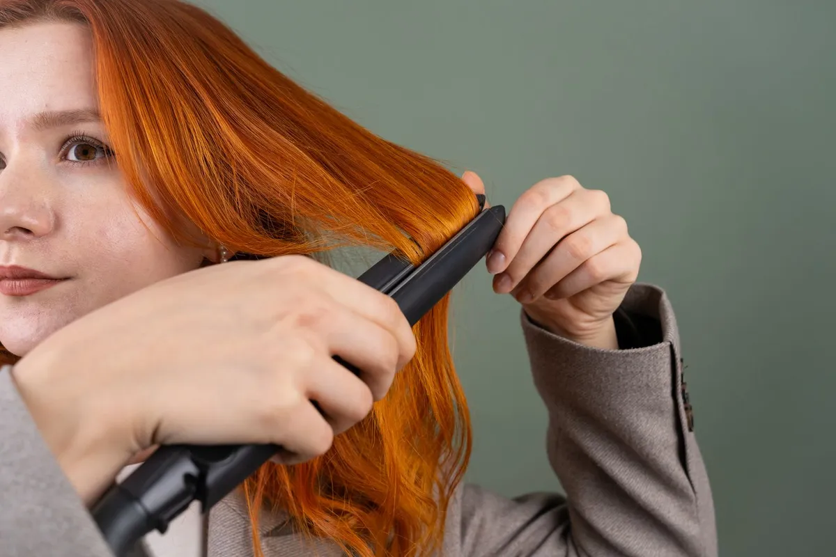 Vrouw stijlt haar lange rode haar met een zwarte stijltang