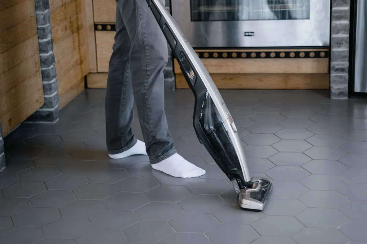 Draadloze steelstofzuiger reinigt een harde tegelvloer in de keuken