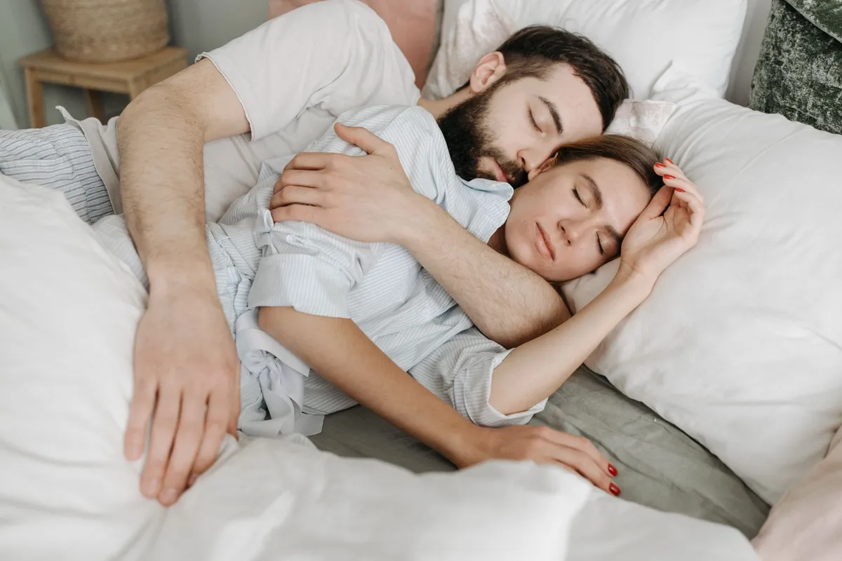 Man en vrouw slapen dicht tegen elkaar aan in het midden van een bed met wit beddengoed