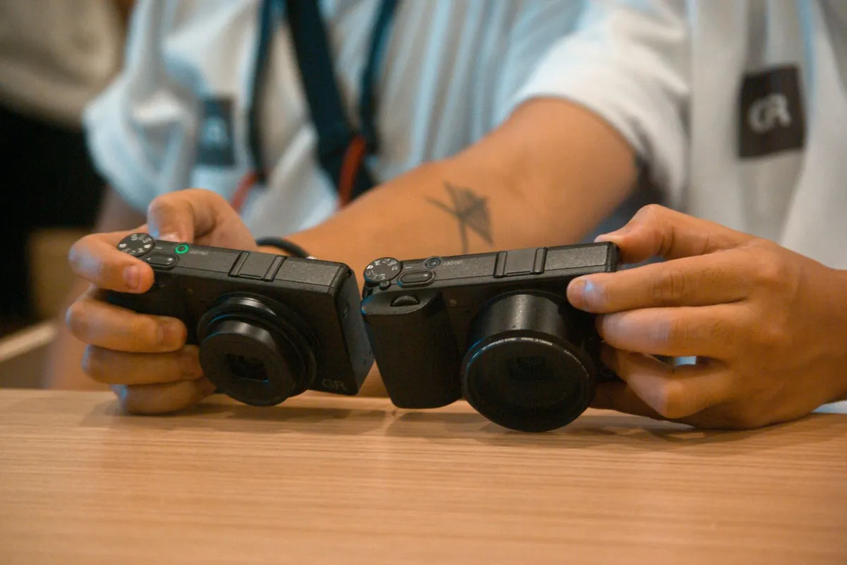 Twee compacte camera's met uitstekende zoomlens naast elkaar in handen op een houten tafel